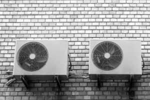Black and white image of three air conditioners on a brick wall